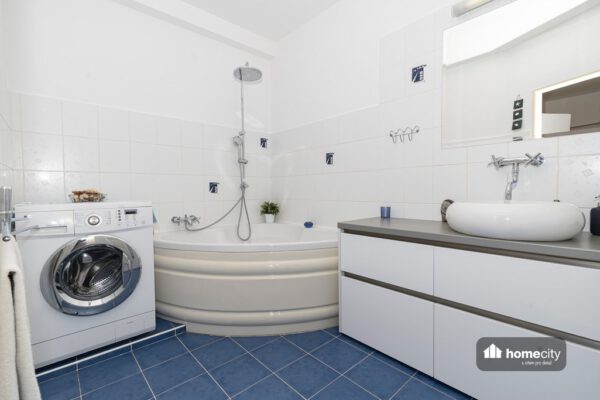 Fotografie koupelny s rohovou vanou, pračkou a umyvadlem